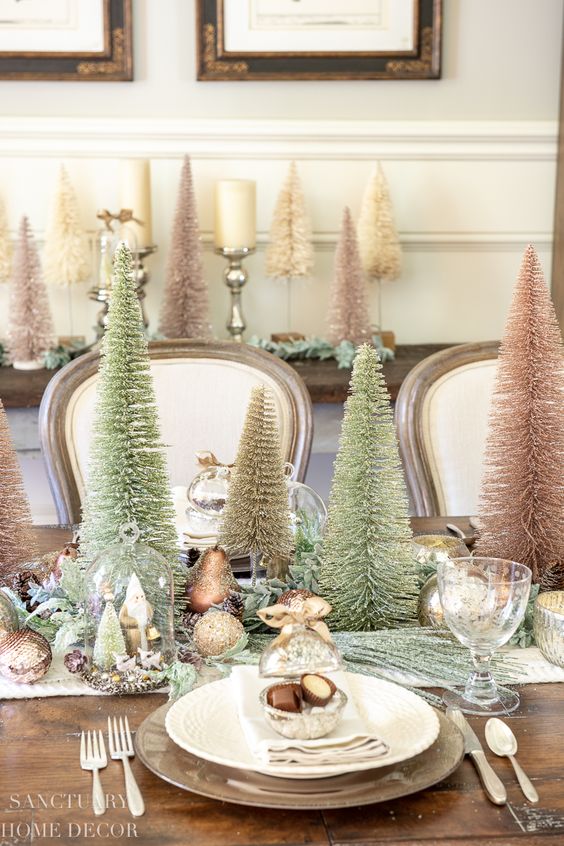 an elegant Christmas tablescape with faux evergreens, bottle brush trees, metallic and glitter ornaments, metallic placemats and chic cutlery