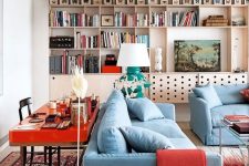 10 a bold living room with a plywood storage unit on the wall, butterflies, blue furniture, a hot red desk behind the sofa and bold red textiles