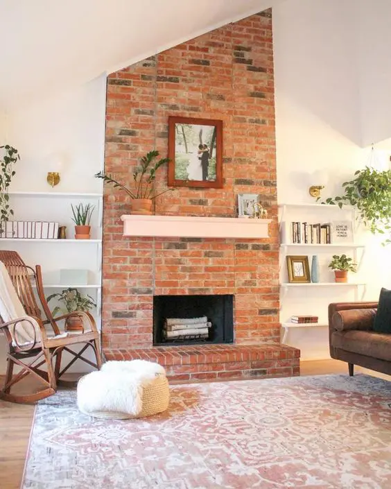 a modern living room with a red brick fireplace, niche shelves, a printed rug, stained and upholstered furniture and potted plants