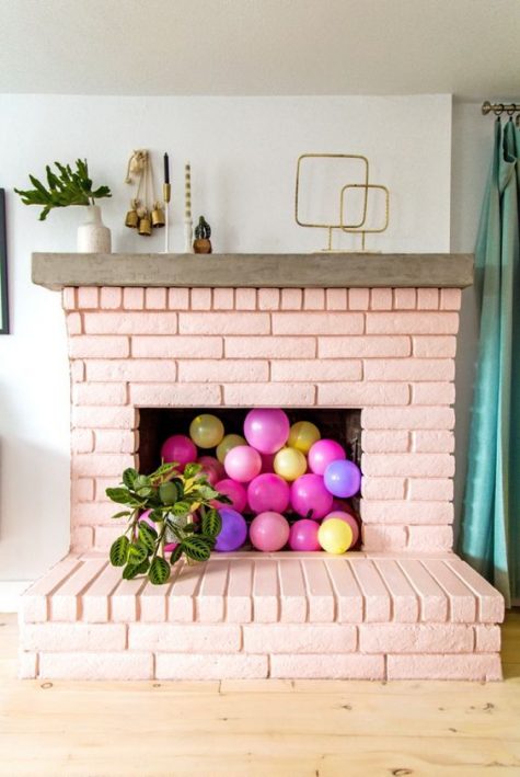 a painted blush brick fireplace filled with colorful balloons and with potted plants all around