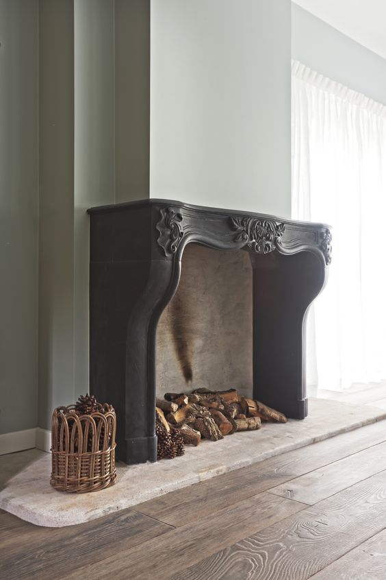 an oversized fireplace with a gorgeous ornated vintage black mantel, with firewood and pinecones inside is fantastic