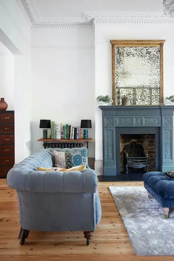 a beautiful neutral living room with a slate grey sofa and a navy ottoman, a vintage fireplace with an oranted grey mantel, an antique mirror over it