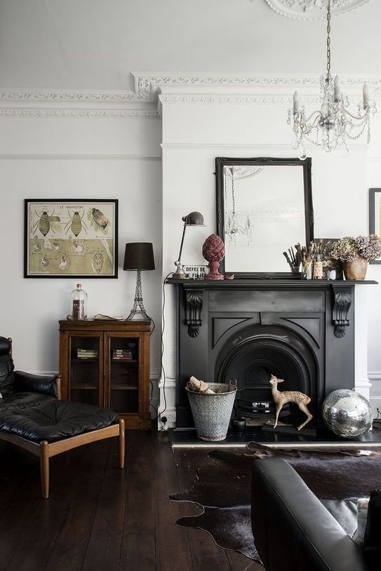 a beautiful vintage living room with a black antique fireplace with a cool mantel, a black elather sofa and lounger, some chic decor and a crystal chandelier