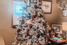14 a flocked Christmas tree with burlap, buffalo check and red plaid ribbons, lights and glitter branches on top plus pinecones