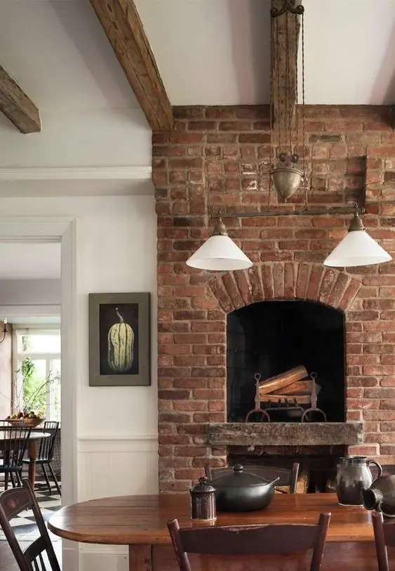 a rustic dining room with a red brick fireplace, rich and dark-stained furniture, modern and vintage pendant lamps