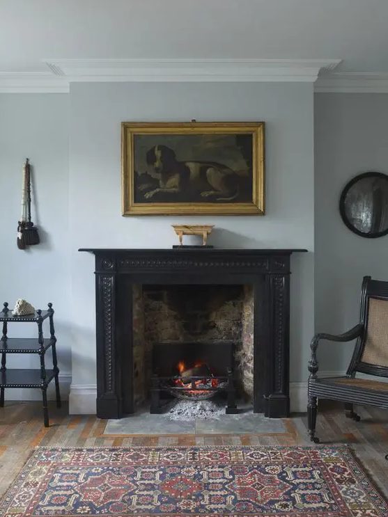 a brick fireplace clad with a vintage black mantel, with a vintage artwork over it and a bold printed rug is pure chic