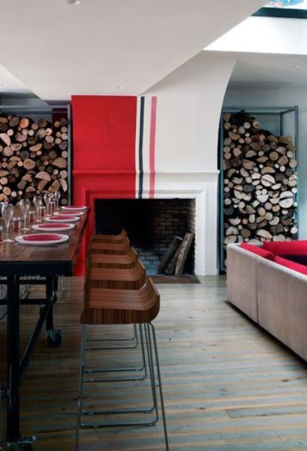 a stylish space with a large fireplace painted hot red and stripes, with a raised dining space, firewood and a sofa with red upholstery