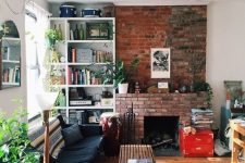 16 a welcoming mid-century modern living room with a red brick fireplace, a black sofa, a stained bench and built-in shelves plus greenery