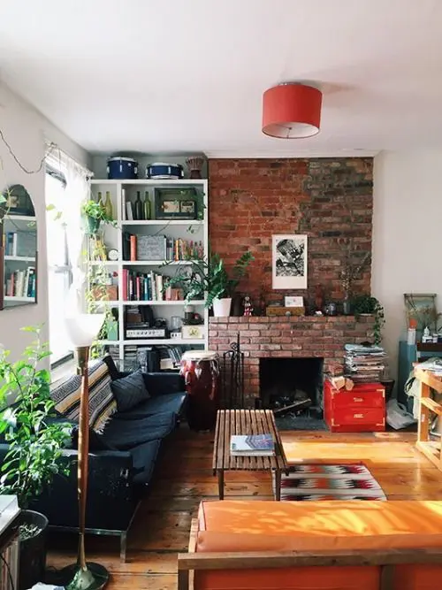 a welcoming mid century modern living room with a red brick fireplace, a black sofa, a stained bench and built in shelves plus greenery