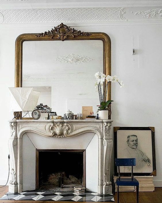 a chic vintage fireplace with an ornated mantel, some pretty mantel decor, an oversized mirror and some books