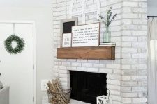 19 a chic whitewashed brick fireplace with a wooden mantel, artworks and eucalyptus, a wire basket with firewood