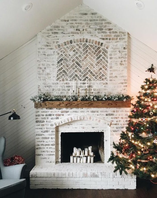 a stylish whitewashed brick fireplace with a wooden mantel with greenery and candles looks very stylish and rustic