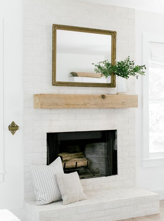 a stylish whitewashed brick fireplace with a wooden mantel, a mirror and greenery plus printed pillows for a cozy feel