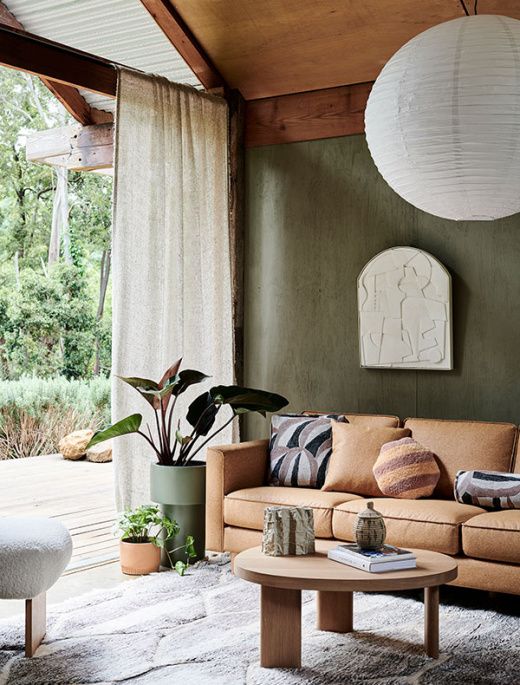 a beautiful sustainable living room with textural green walls, wooden furniture, potted plants, a leather sofa and textural rugs