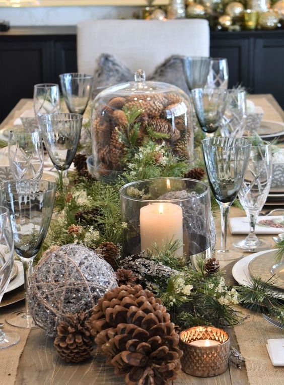 a chic forest Christmas tablescape with evergreens, small and large pinecones, candles, smoked glasses and a shiny twine ball