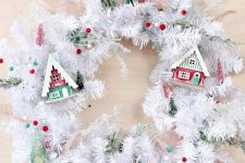 23 a white evergreen Christmas wreath with colorful pompoms, colorful small houses and bottle brush Christmas trees