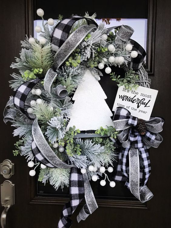 a Christmas wreath with shiny silver and buffalo check ribbons, faux evergreens, berries, a plywood tree and a sign