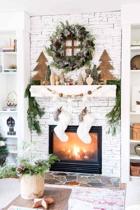 a forest Christmas mantel with faux trees, wooden beads, greenery and evergreens, a snowy pinecone wreath and white stockings