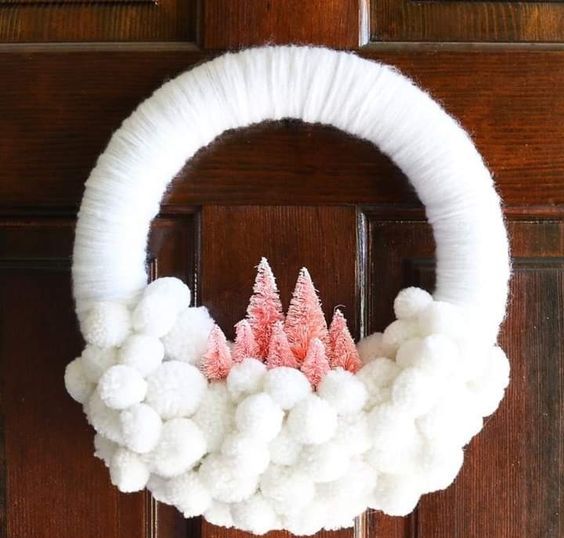 a white yarn and pompom Christmas wreath with pink bottle brush trees is a soft and lovely decor idea for a neutral space