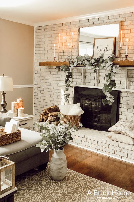 a large whitewashed brick fireplace, a stained mantel with greenery, a mirror and art plus candles