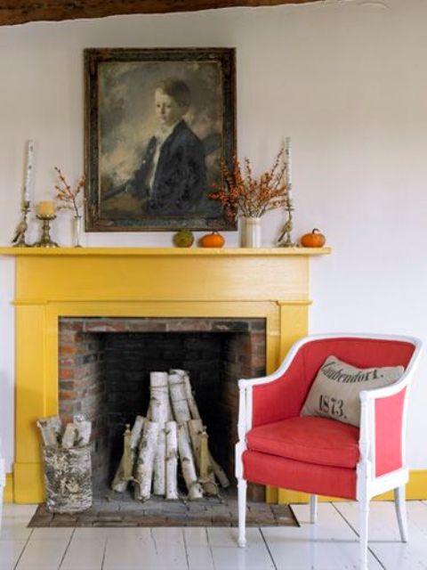 a red brick fireplace clad with a bold yellow mantel and a bright red and white vintage chair, some vases and candleholders