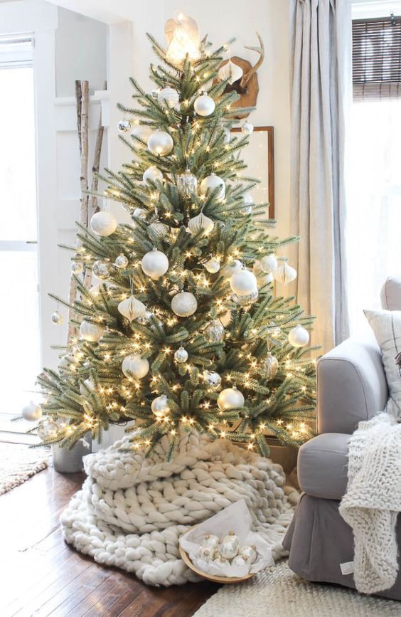 a simple and stylish Christmas tree with white and silver ornaments, lights and a white chunky knit cover for the base