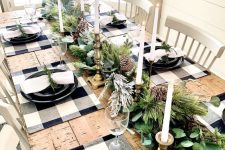 27 a natural Christmas table setting with buffalo check placemats, black plates, an evergreen garland with pinecones and candles