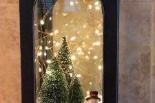 28 a black metal lantern with faux snow, bottle brush Christmas trees, lights and a small snowman is a lovely idea