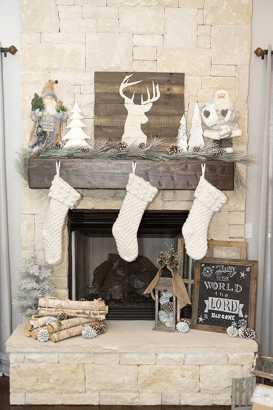 a woodland Christmas mantel with white stockings, snowy evergreens and pinecones, a deer silhouette, firewood and faux trees