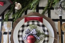 28 an elegant holiday place setting with a buffalo check plate and a red ornament, some evergreens and elegant cutlery
