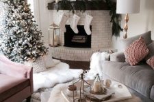 29 a Christmas living room with a whitewashed brick fireplace and a mantel dressed up with evergreens, a gorgeous tree and faux fur