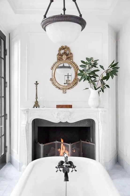 an exquisite white bathroom with a glazed wall, a bathtub, a vintage fireplace wiht a chic white mantel and a metal screen is amazing