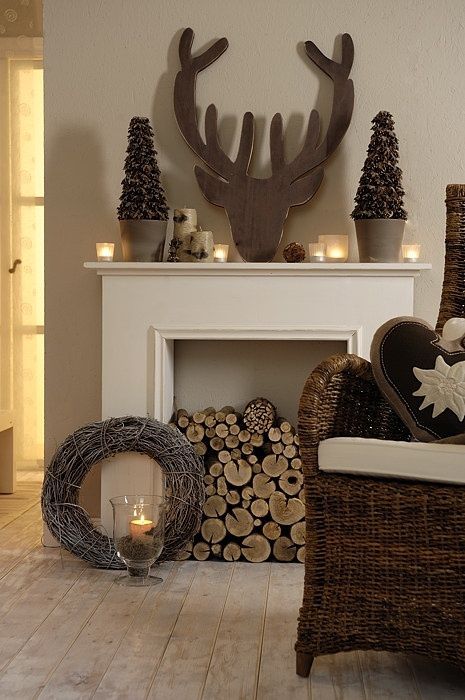 elegant woodland Christmas decor with a deer head silhouette, mini potted trees, candles and pillar candles, firewood in the fireplace and a simple vine wreath