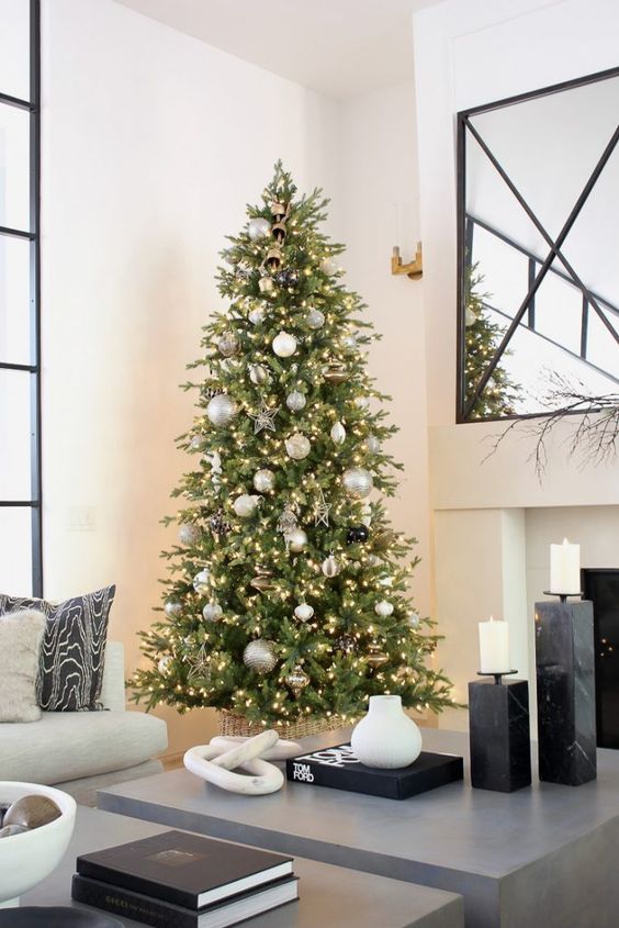 a shiny Christmas tree with white, silver, gold and black ornaments, lights, shiny stars and rold ribbon is modern and glam