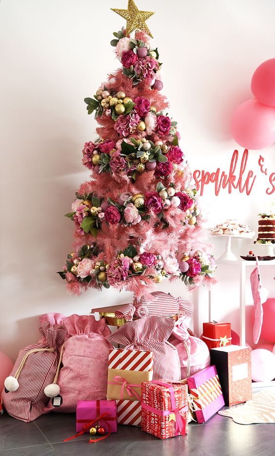 a girlish pink Christmas tree decorated with pink and gold ornaments, with pink faux blooms and leaves plus a gold star on top