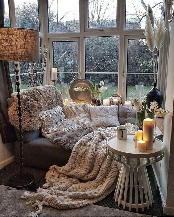 a gorgeous window nook with a daybed styled with lots of textural pillows and blankets, pampas grass and a lamp with a burlap shade