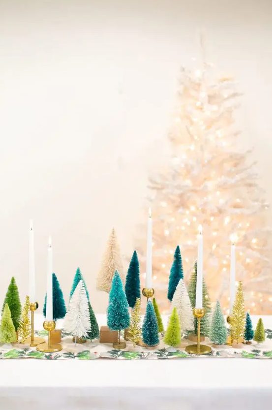 a Christmas table with a printed runner, white, green, teal and gold bottle brush Christmas trees and candles
