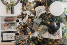 a Christmas tree decorated with small black and large white ornaments, lights, greenery and plaid ribbons is a chic idea