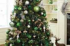 a Christmas tree with light green and emerald ornaments, silver and gold ones, lights, leaves and a large silver glitter star on top