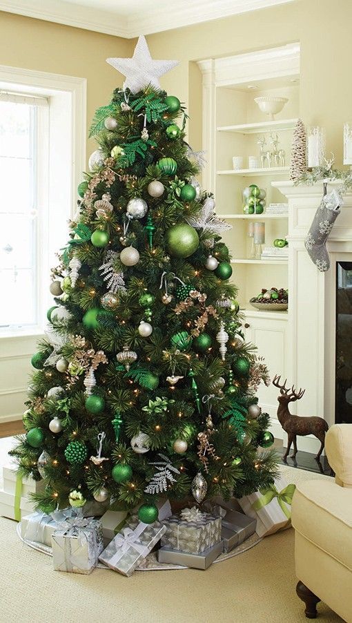 a Christmas tree with light green and emerald ornaments, silver and gold ones, lights, leaves and a large silver glitter star on top
