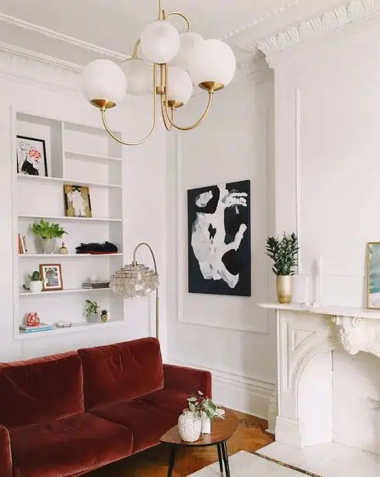 a beautiful Parisian styled living room with ornated crown molding, a non working fireplace, a burgundy velvet sofa and built in niche shelves