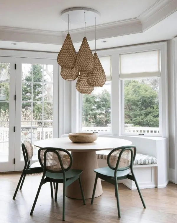 a beautiful breakfast nook with a rounded banquette seating with striped upholtsery, a round table, green chairs and a cluster of pendant lamps