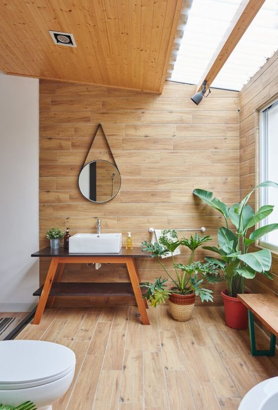 a beautiful modern bathroom clad with wood all over, with a large skylight, lots of potted plants and mid-century modern furniture of wood