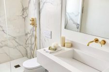 a breathtaking white marble bathroom with marble in the shower space, a white slab sink, white appliances and gold fixtures