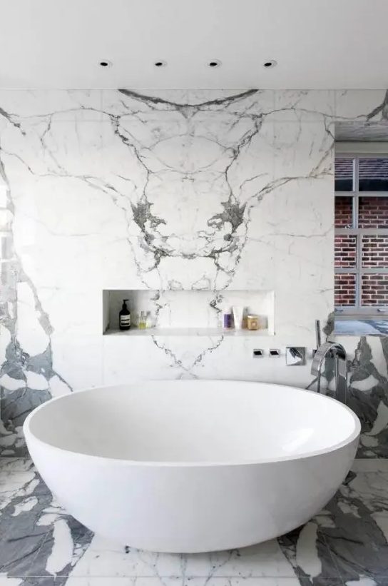 a bright contemporary bathroom done with white and grey tiles, a modern oval tub and windows