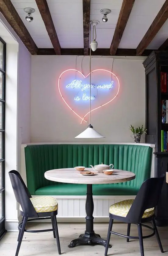 a bright dining space with a green banquette seating, elegant black chairs, a round table and a gorgeous neon sign