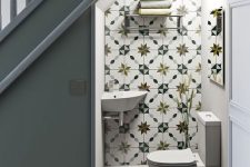 a catchy under stair bathroom with white and printed tiles, white appliances and a small metal shelf for towels