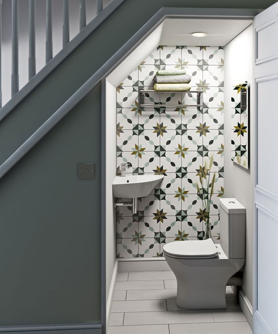 a catchy under stair bathroom with white and printed tiles, white appliances and a small metal shelf for towels