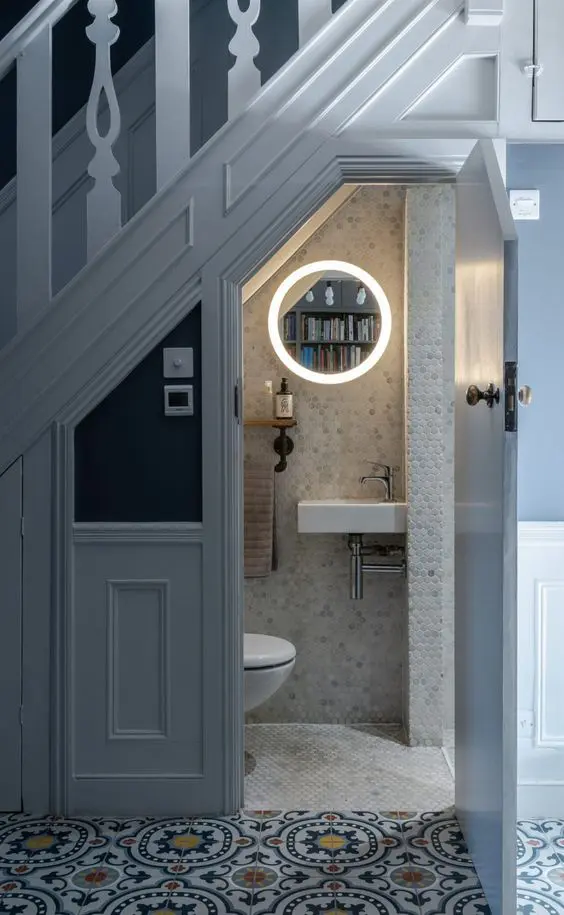 a catchy under stari powder room clad with marble penny tiles, white appliances, a lit up mirror, an industrial shelf and neutral towels