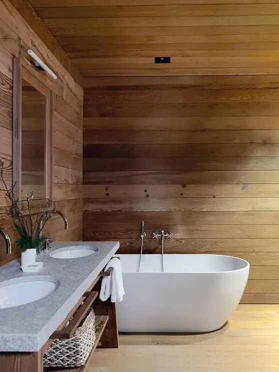 a chalet bathroom clad with wood completely, with an oval tub, a wooden vanity with a double sink is very simple and very inviting